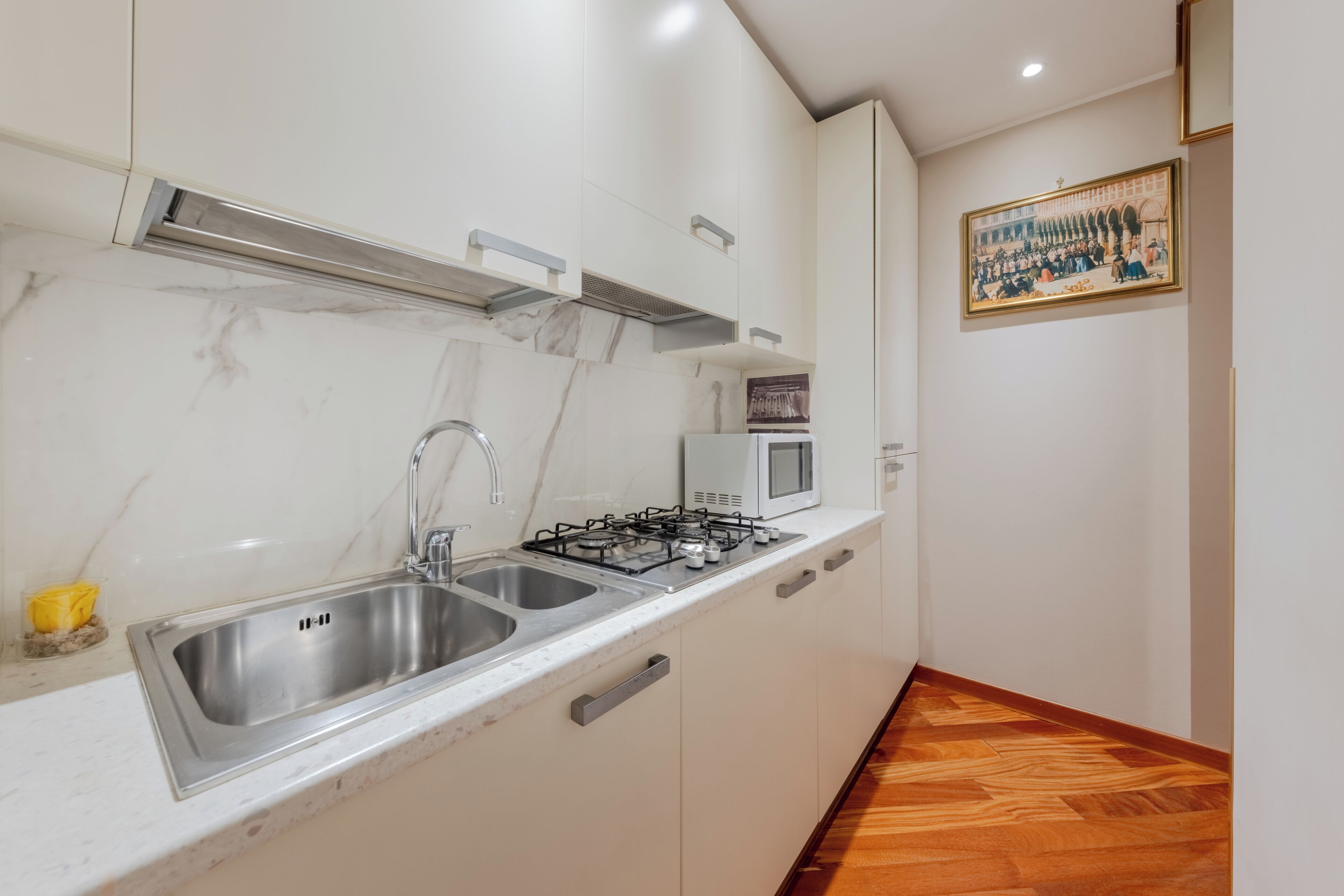 Una cocina con armarios blancos, un lavamanos de acero inoxidable, una estufa a gas y un microondas.