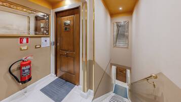 A hotel hallway with a fire extinguisher, a wooden door, a mirror, a window, and a staircase.