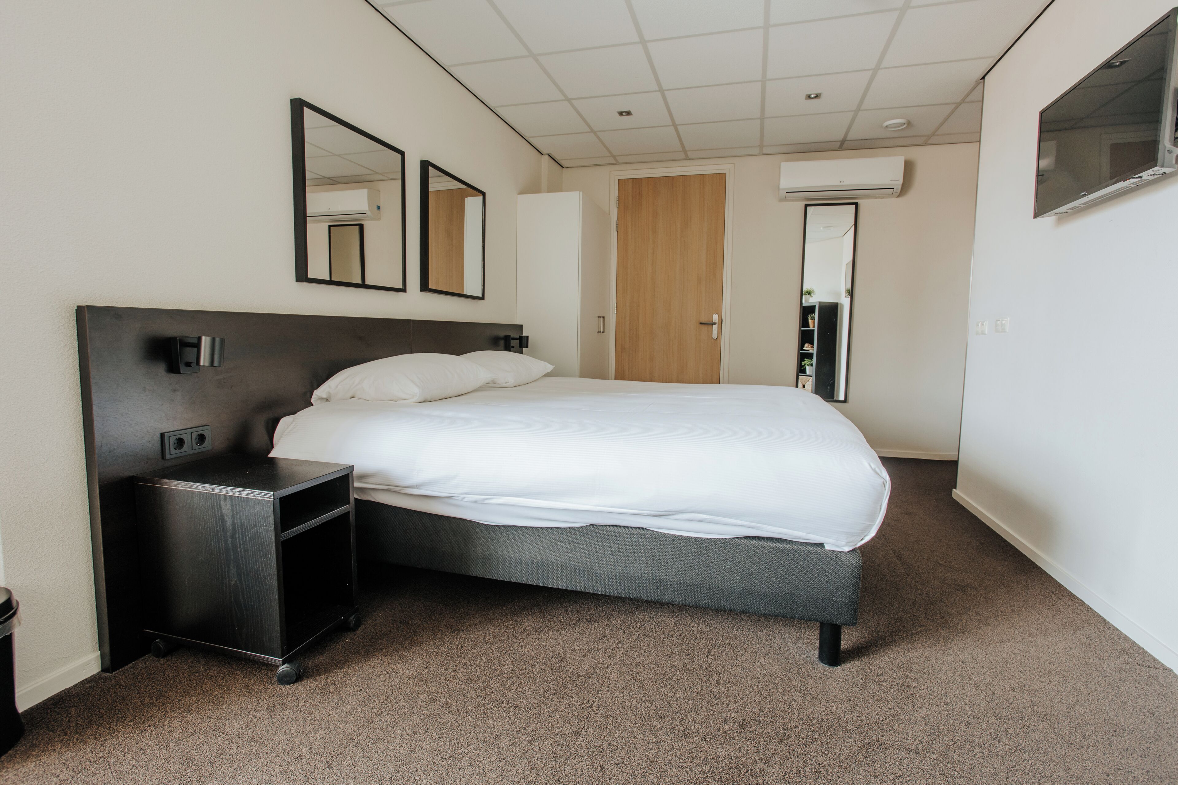 Una habitación de hotel con una cama, una mesita de noche, un espejo y un armario.