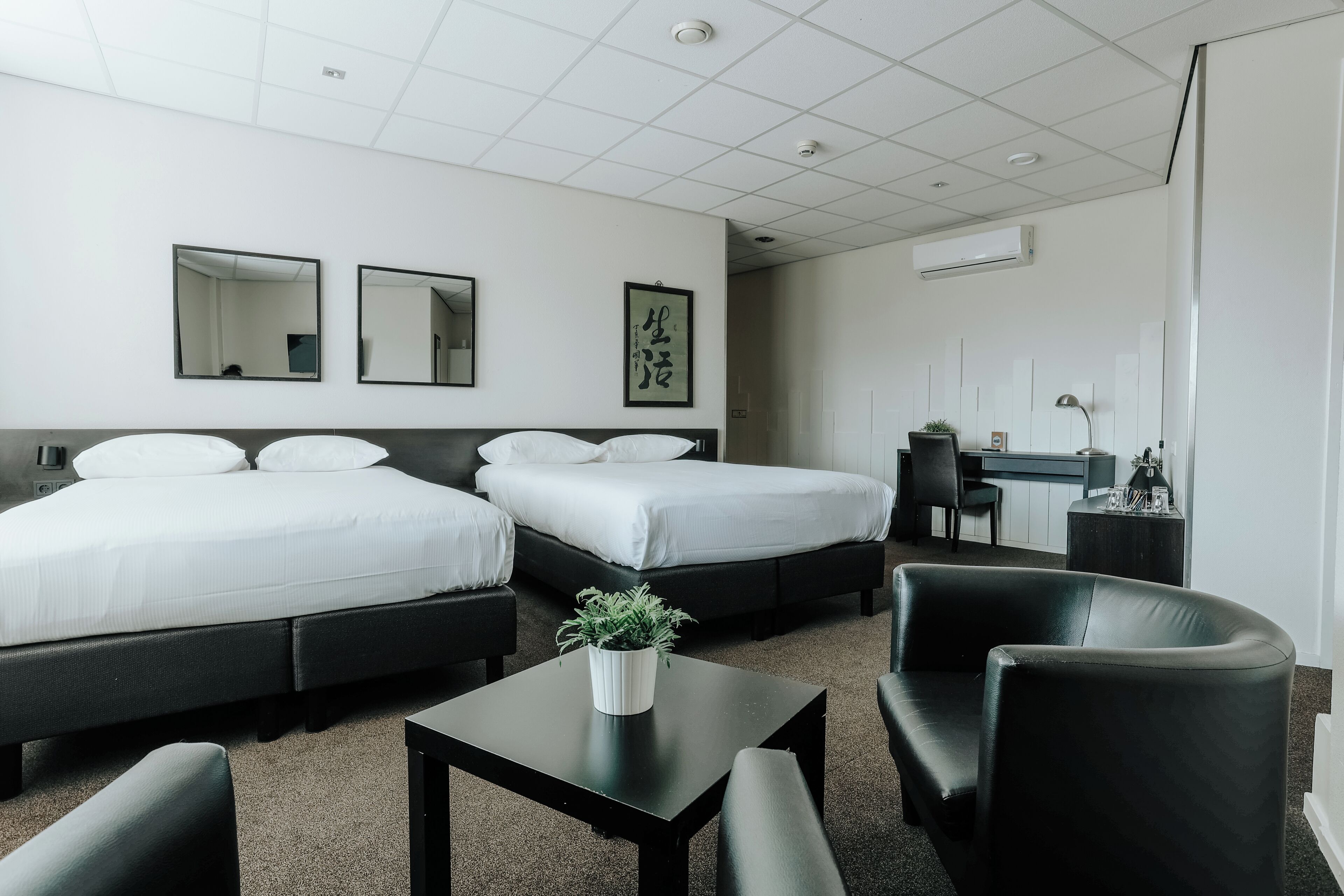 Habitación de hotel con dos camas, un escritorio, una silla y una mesita con una planta.