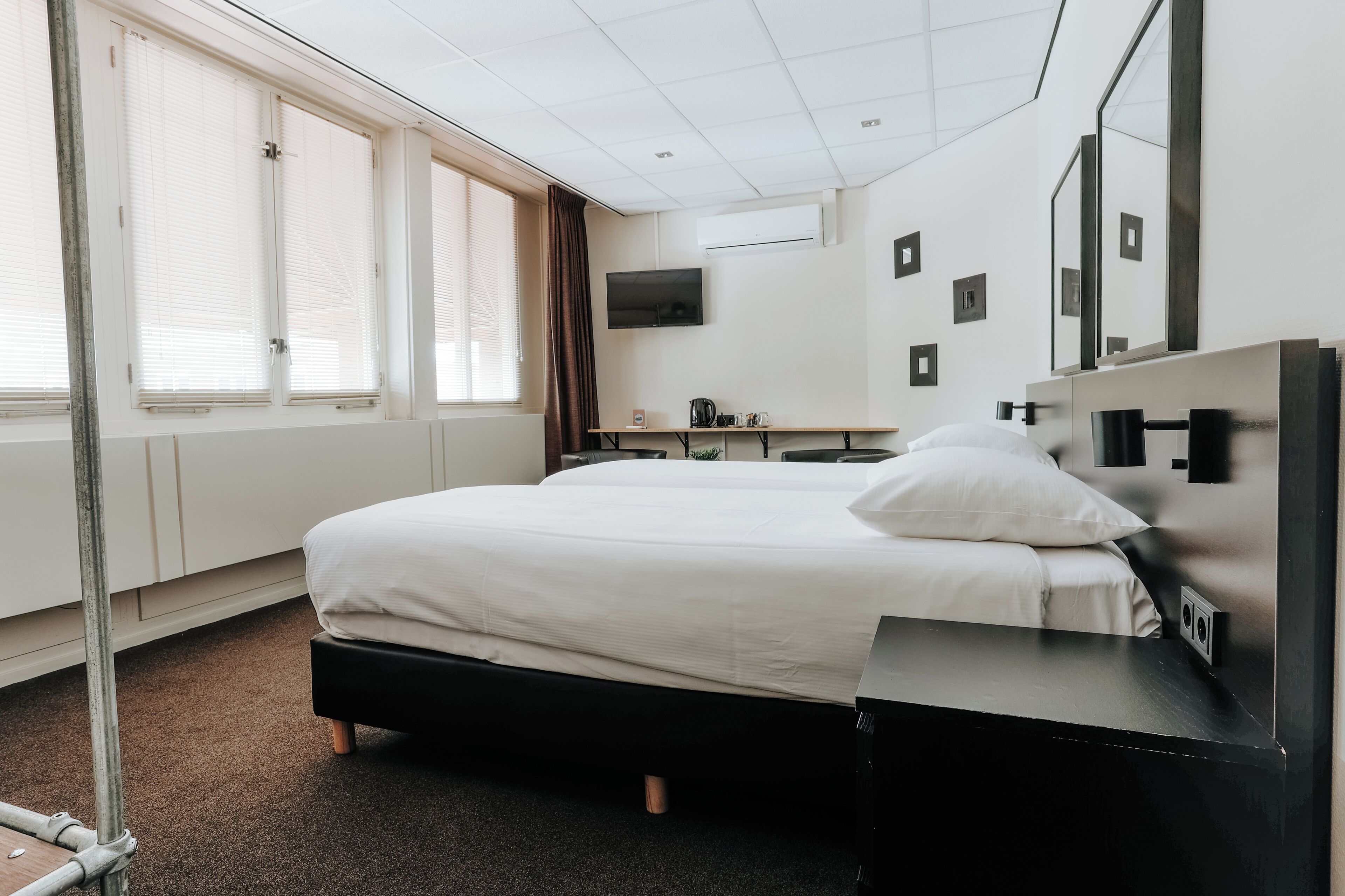 A hotel room with a bed, a desk, a TV, and a window with blinds.