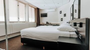 A hotel room with a bed, a desk, a TV, and a window with blinds.