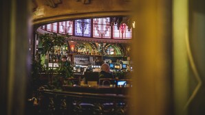 Een bar met een ronde indeling, met een glas-in-loodraam en diverse flessen en glazen op planken.