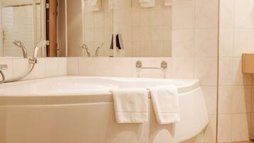 A modern bathroom with a large bathtub, a mirror, and a towel rack.