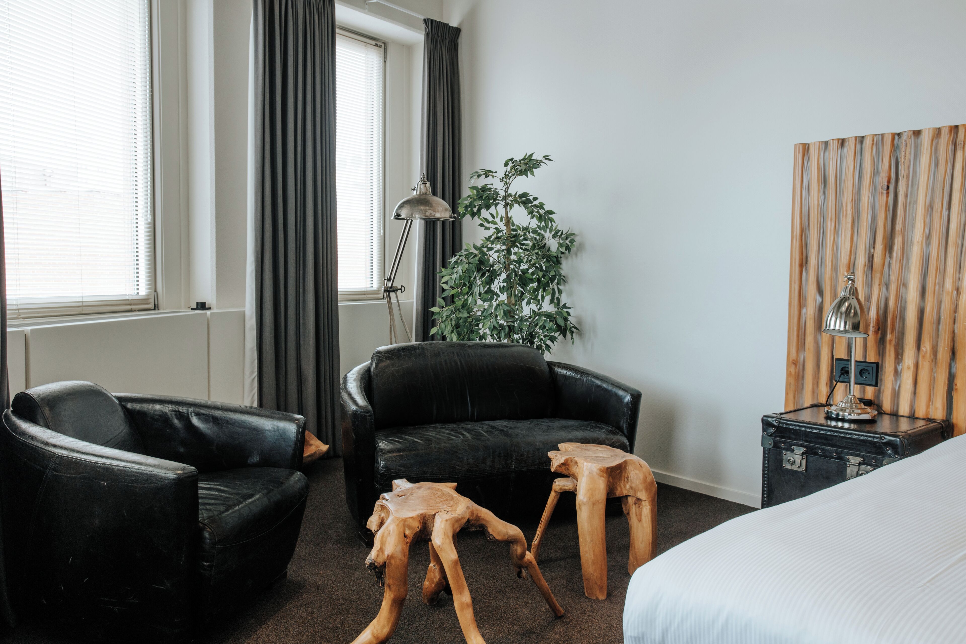 A hotel room with a black leather sofa, a wooden coffee table, a potted plant, a lamp, and a bed.