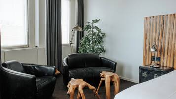 A hotel room with a black leather sofa, a wooden coffee table, a potted plant, a lamp, and a bed.