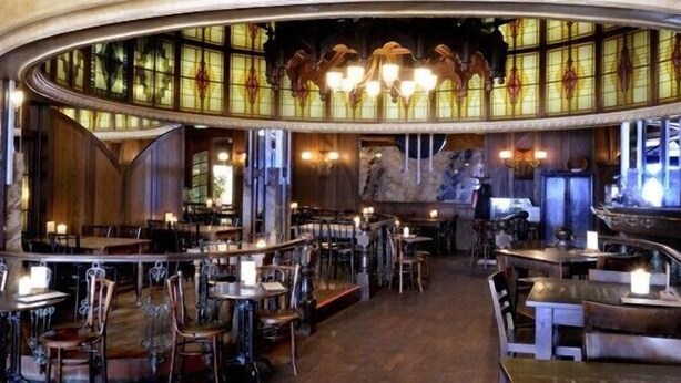 Een restaurant met een gebogen plafond, glas-in-loodramen en meerdere tafels en stoelen.