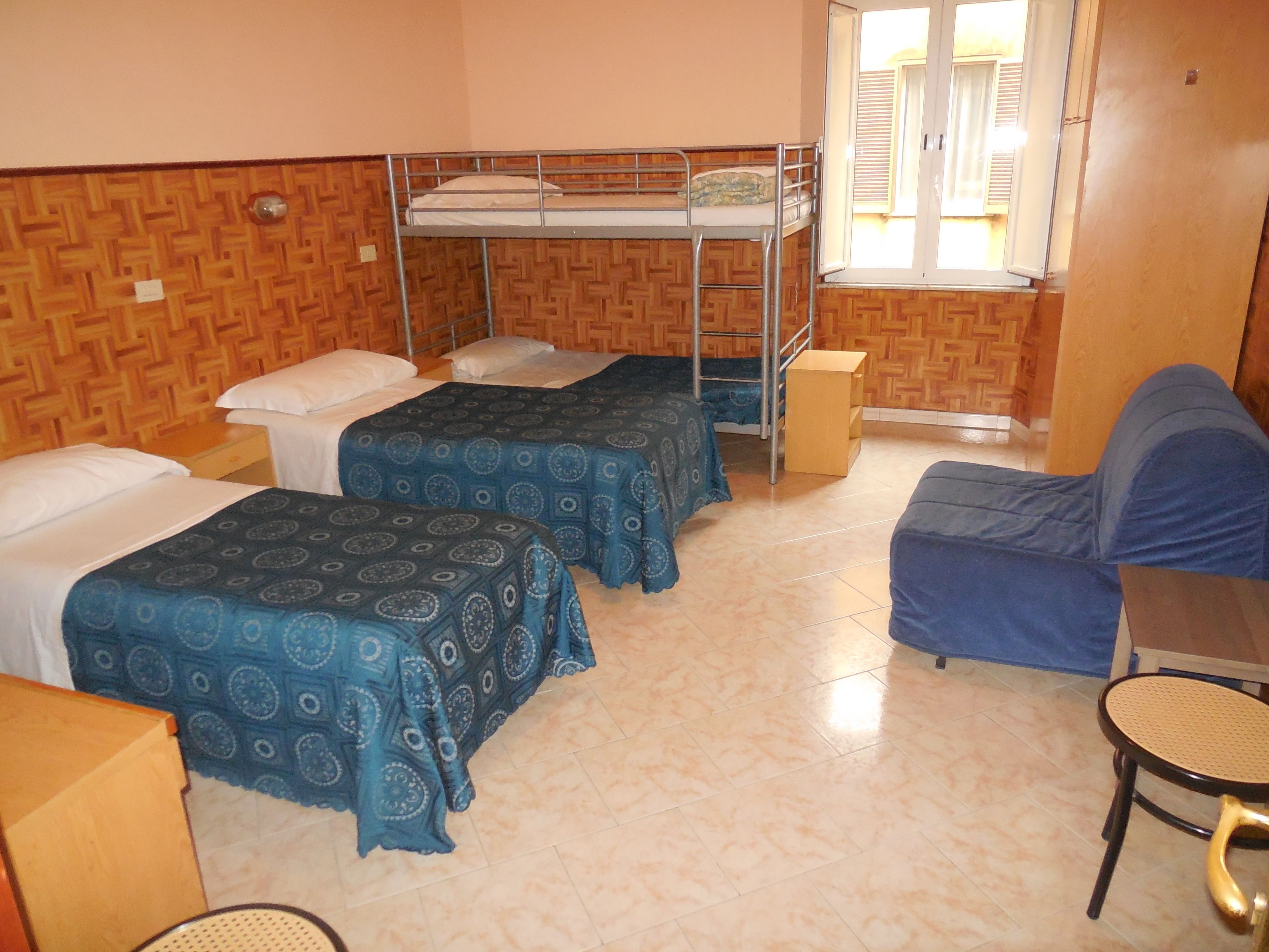 Quarto com duas camas de solteiro, uma beliche, um sofá e uma mesinha.