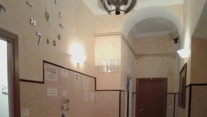 A hallway with a wall clock, a bulletin board, and a small table with a red stool. - Cressy (Rome)