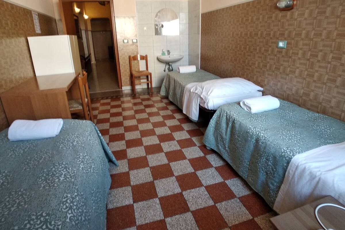 Hotellihuone, jossa on kaksi erillistä sänkyä, pieni työpöytä, tuoli, pesuallas ja peili.