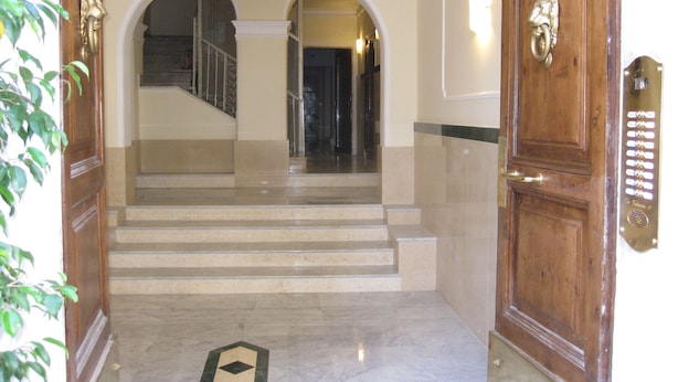 A grand entrance with a marble staircase, a wooden door with a brass handle, and a metal intercom system. - Cressy (Rome)