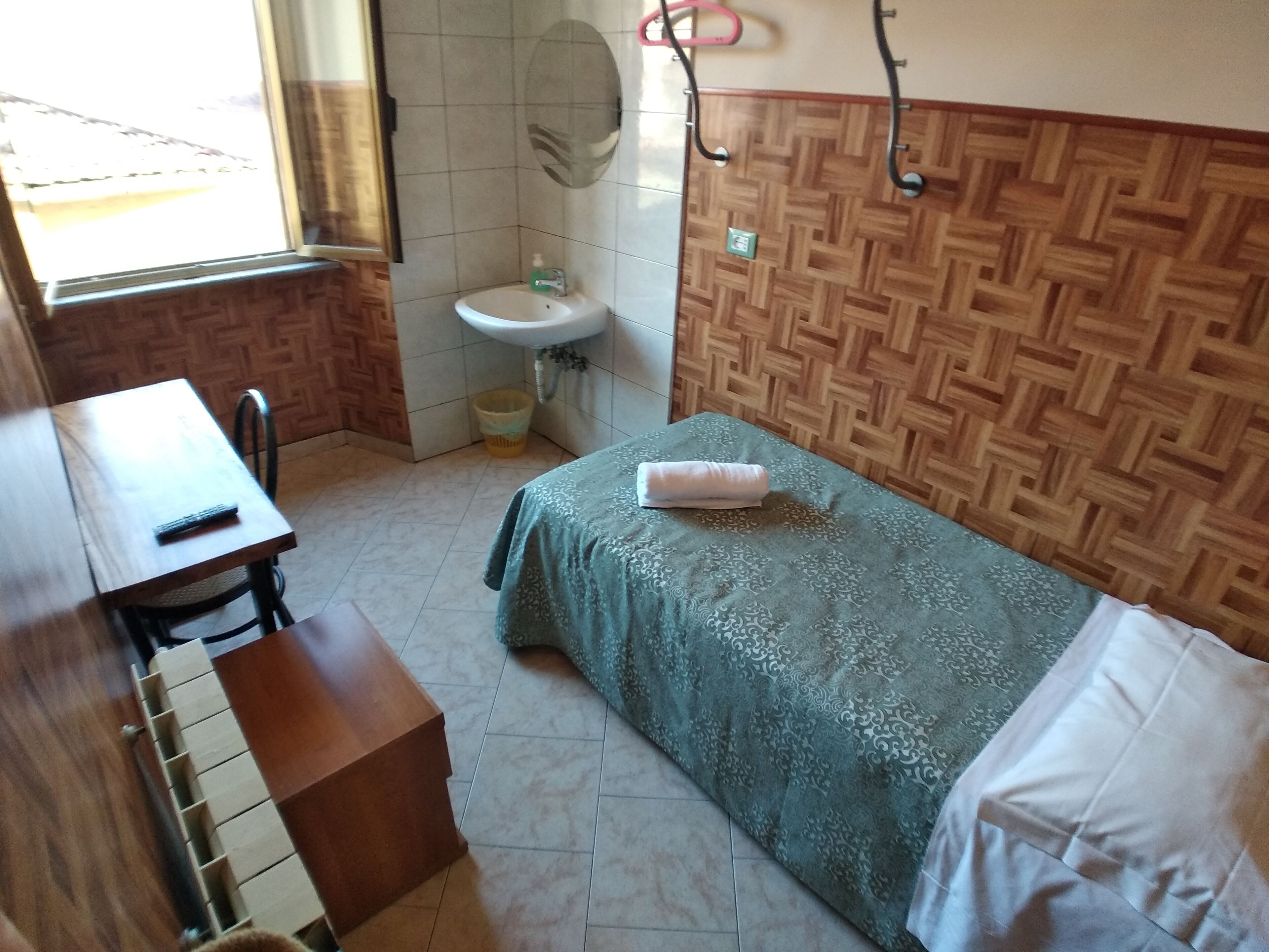 Quarto pequeno e organizado com cama, escrivaninha e pia.