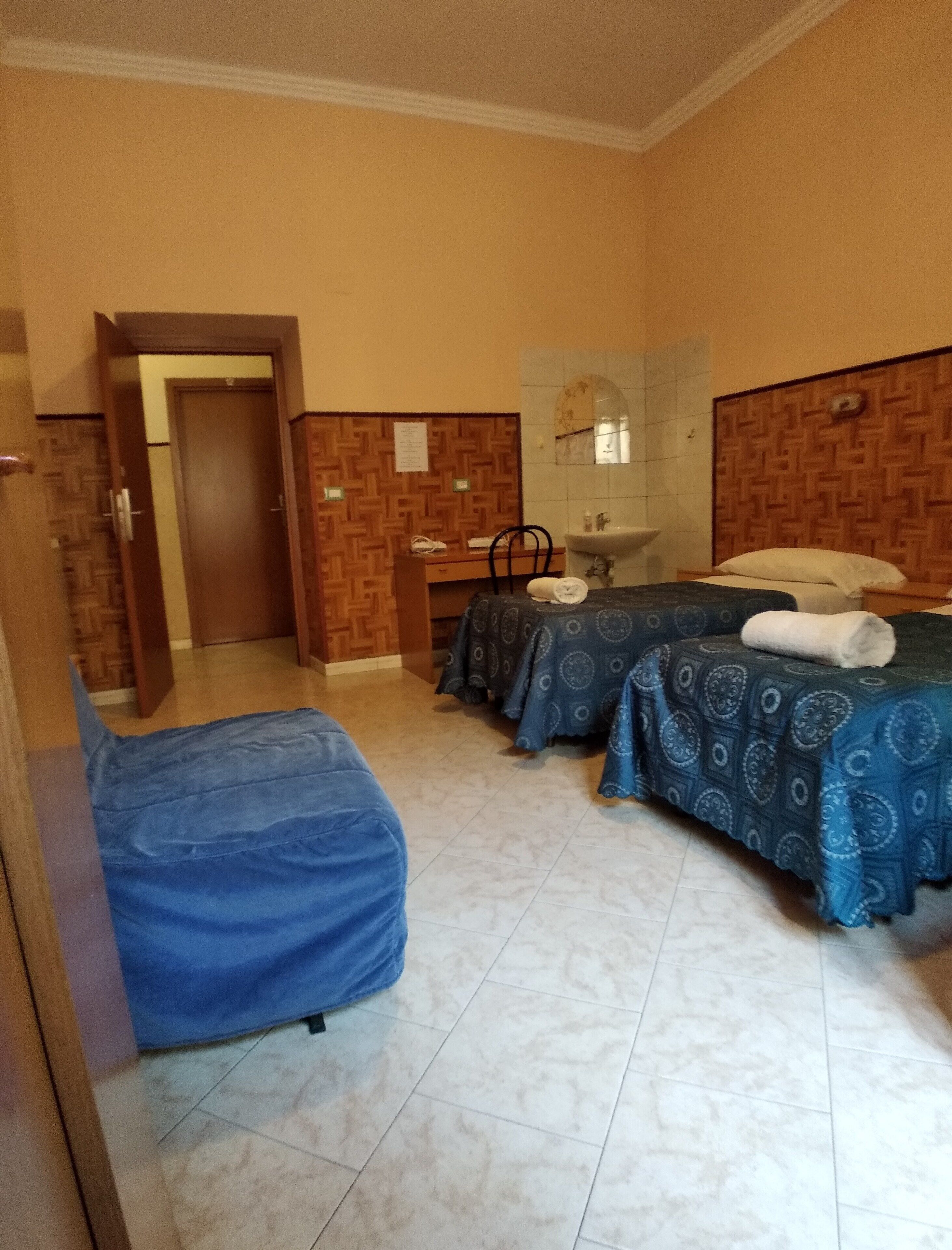 Ein Hotelzimmer mit zwei Betten, einem Schreibtisch, einem Stuhl, einem Waschbecken und einem Spiegel.