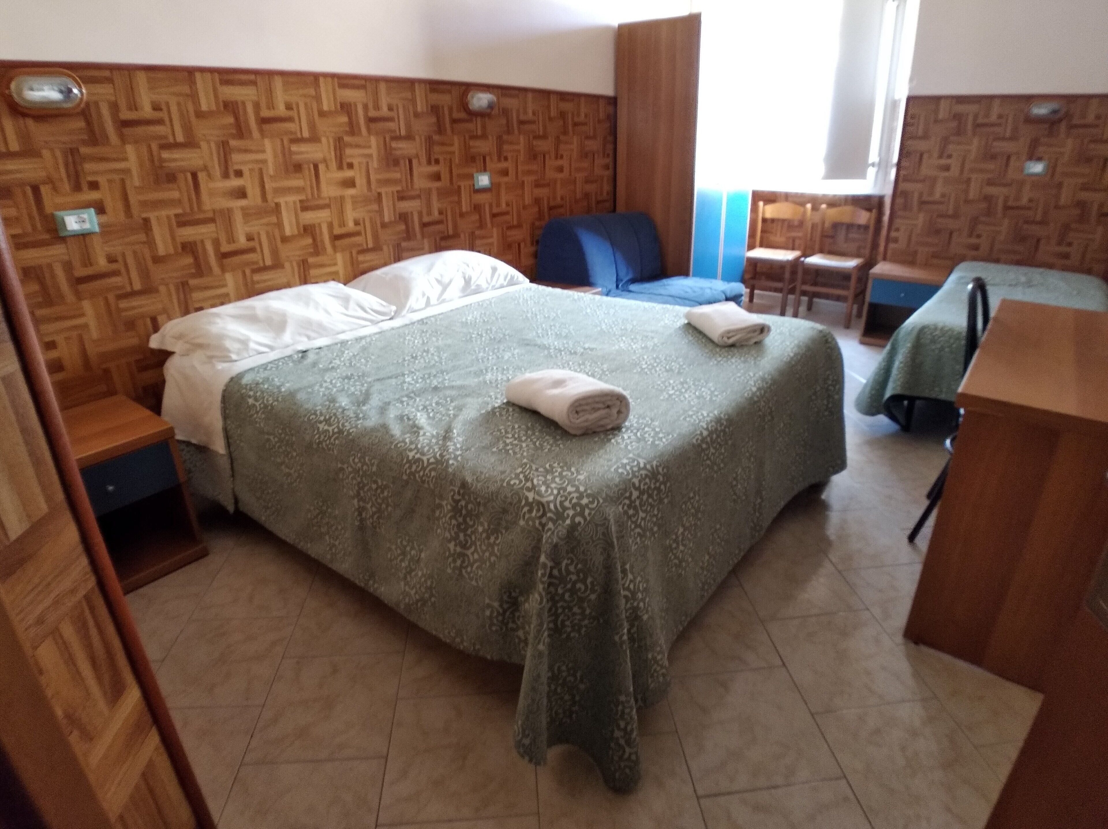 A room with a bed, a chair, a desk, and a wooden wall pattern.