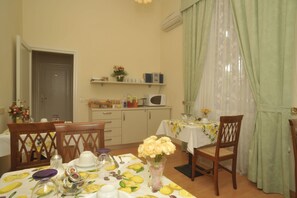 Un comedor con una mesa preparada para dos, microondas y estante con utensilios de cocina.