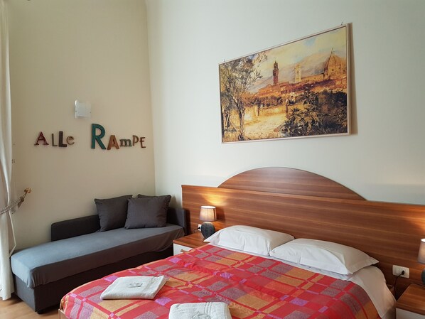 A hotel room with a bed, a sofa, a painting of a cityscape, and a wall with the text "ALLE RAMP". - Villa Alle Rampe (Florence)