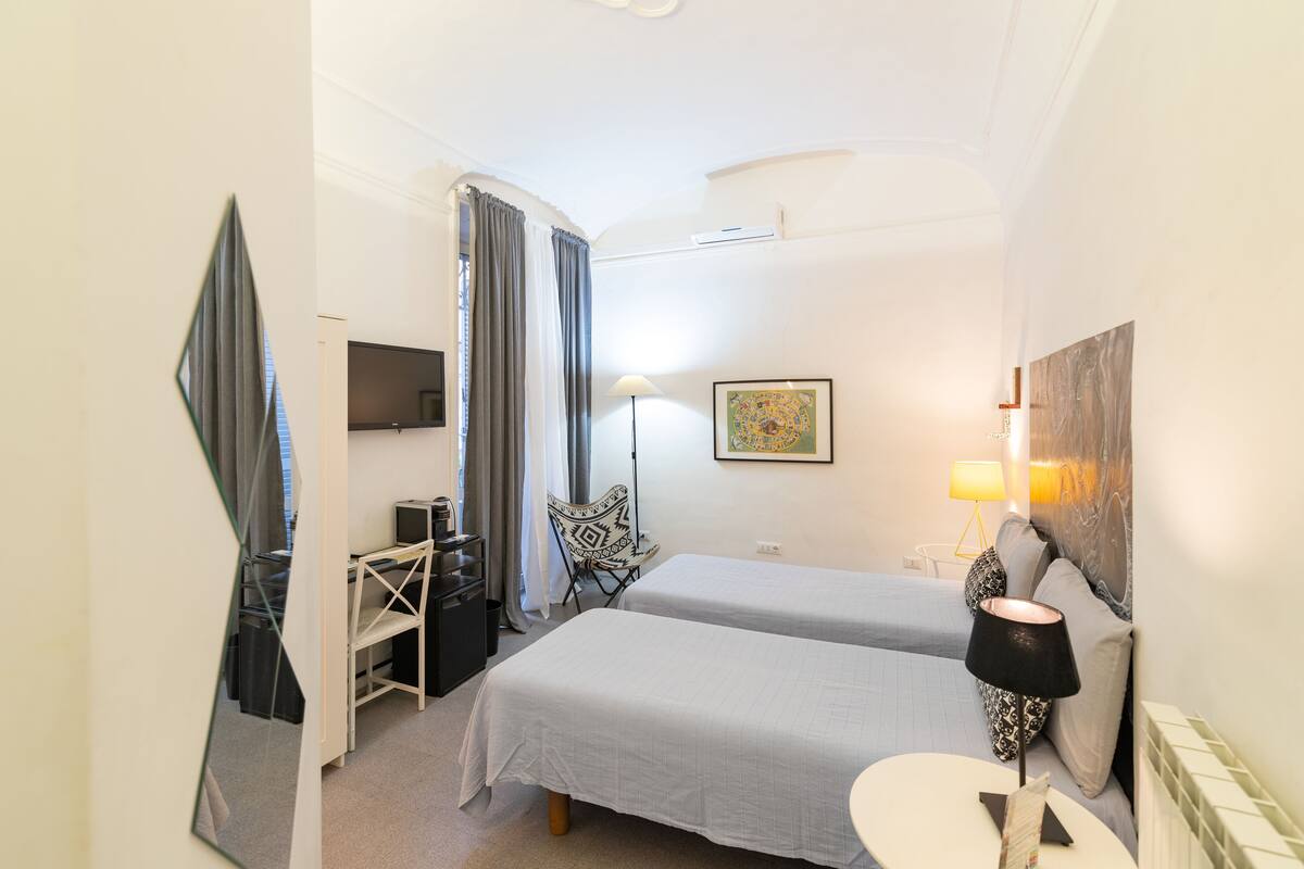 A hotel room with two beds, a desk with a chair, a TV, a lamp, and a painting on the wall.