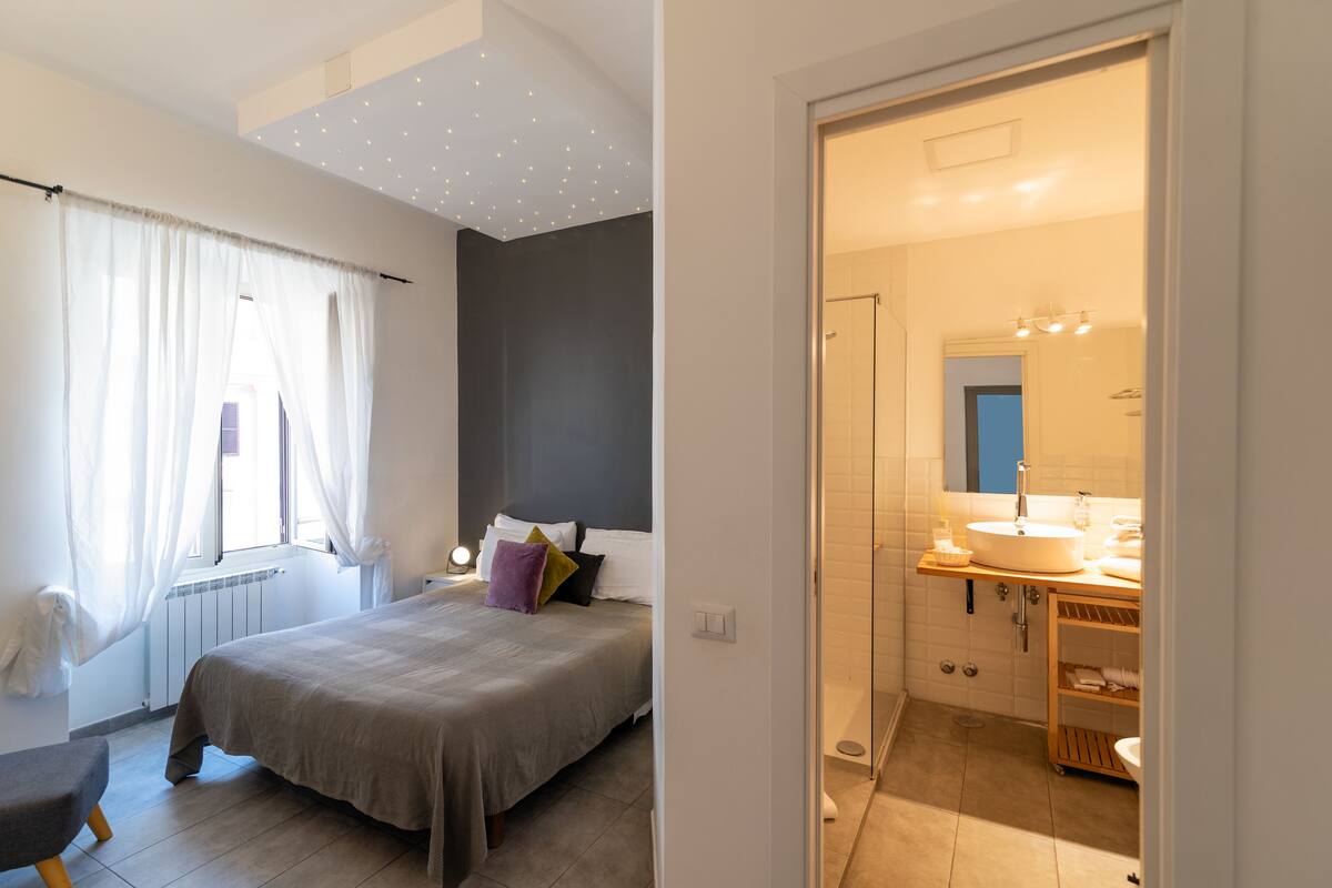 A bedroom with a bed, bedside table, and a window with curtains.