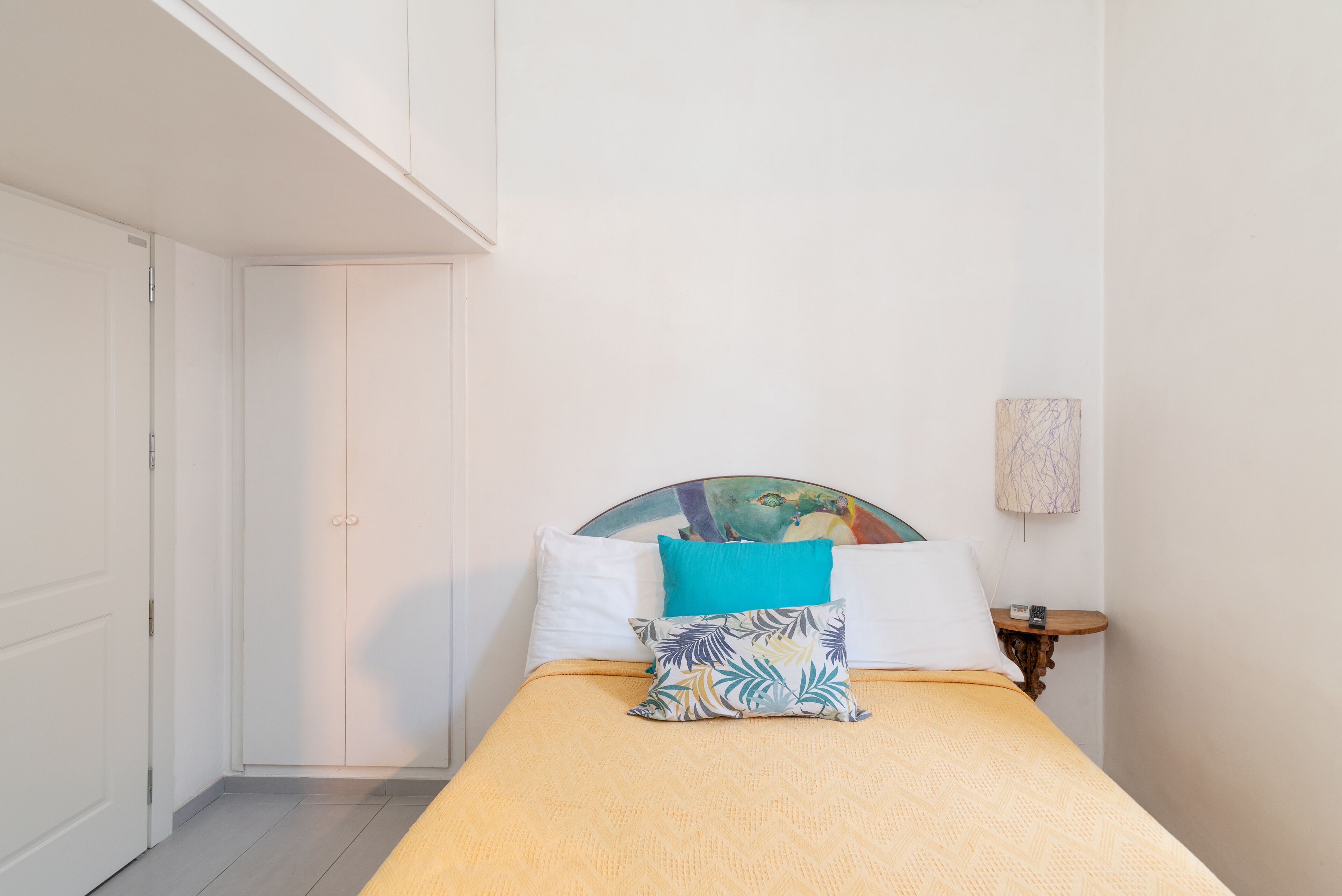A bedroom with a bed, a nightstand, a wall-mounted lamp, and a door.