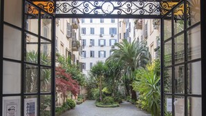 An open doorway with a wrought iron gate leading to a courtyard with cobblestone paths, surrounded by greenery and buildings in the background. - La Casa di Amy (Rome)