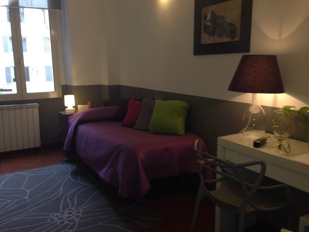 Une chambre à coucher avec un lit, un bureau, une chaise, une lampe et une fenêtre.