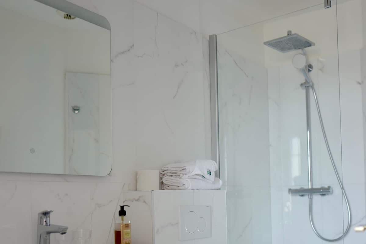 Une salle de bain moderne avec un mur recouvert de carreaux de marbre, un meuble-lavabo en bois, des toilettes blanches et une douche séparée par une paroi en verre.