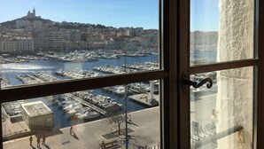 Marina con barcos amarrados, un paisaje urbano al fondo y vista a través de una ventana con marco de madera.