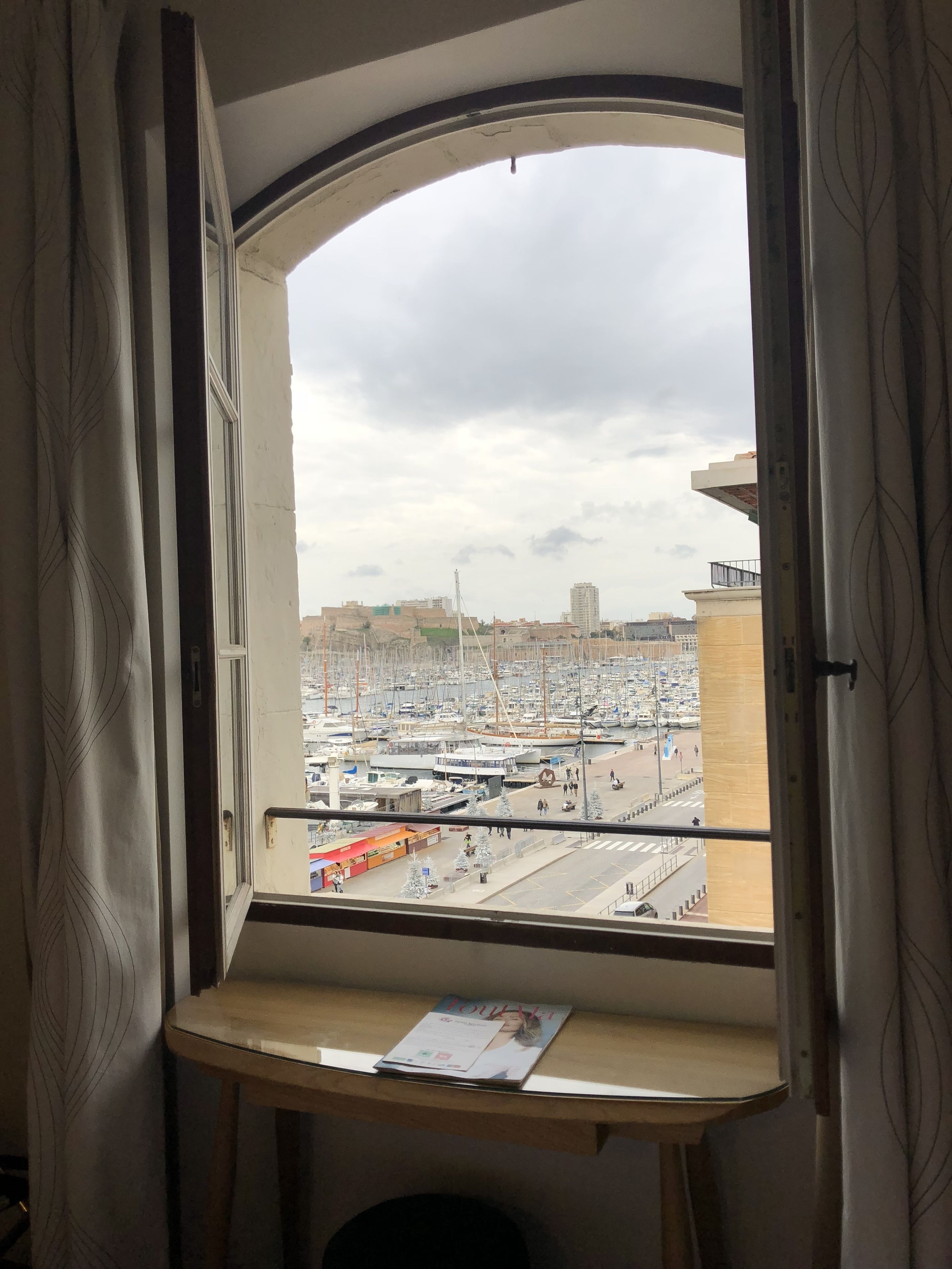 A room with a window overlooking a marina with boats and buildings.