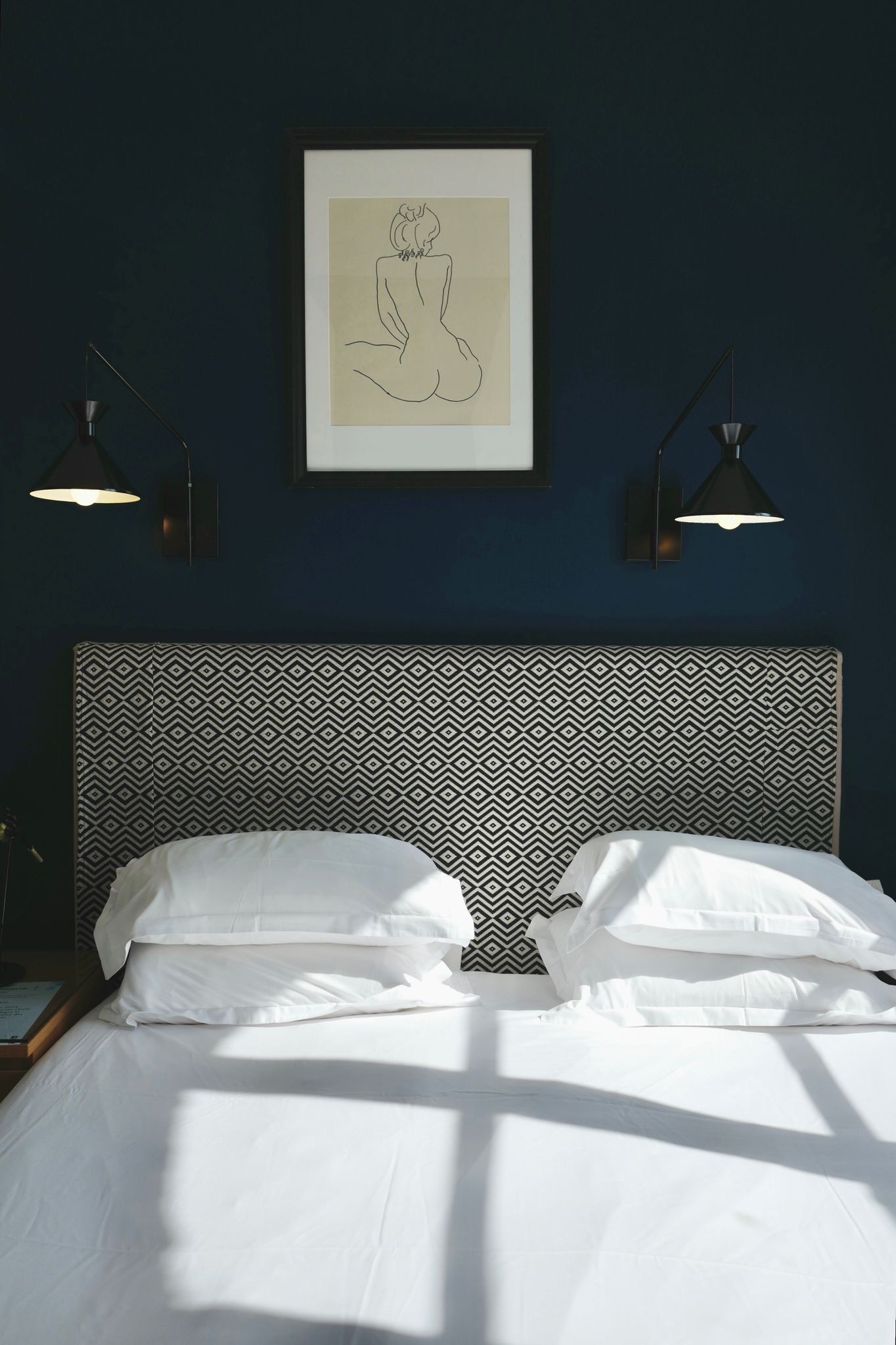 A neatly made bed with white linens, a patterned headboard, and a framed artwork above it.