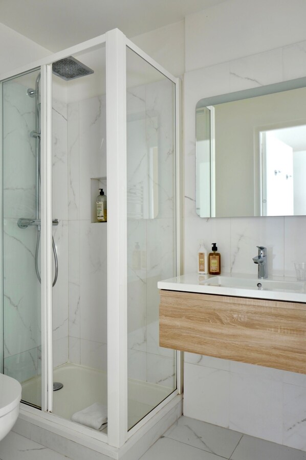 A modern bathroom with a glass-enclosed shower, a white marble-tiled wall, a wooden vanity, and a large mirror. - Hotel Bellevue Marseille (Marseille)