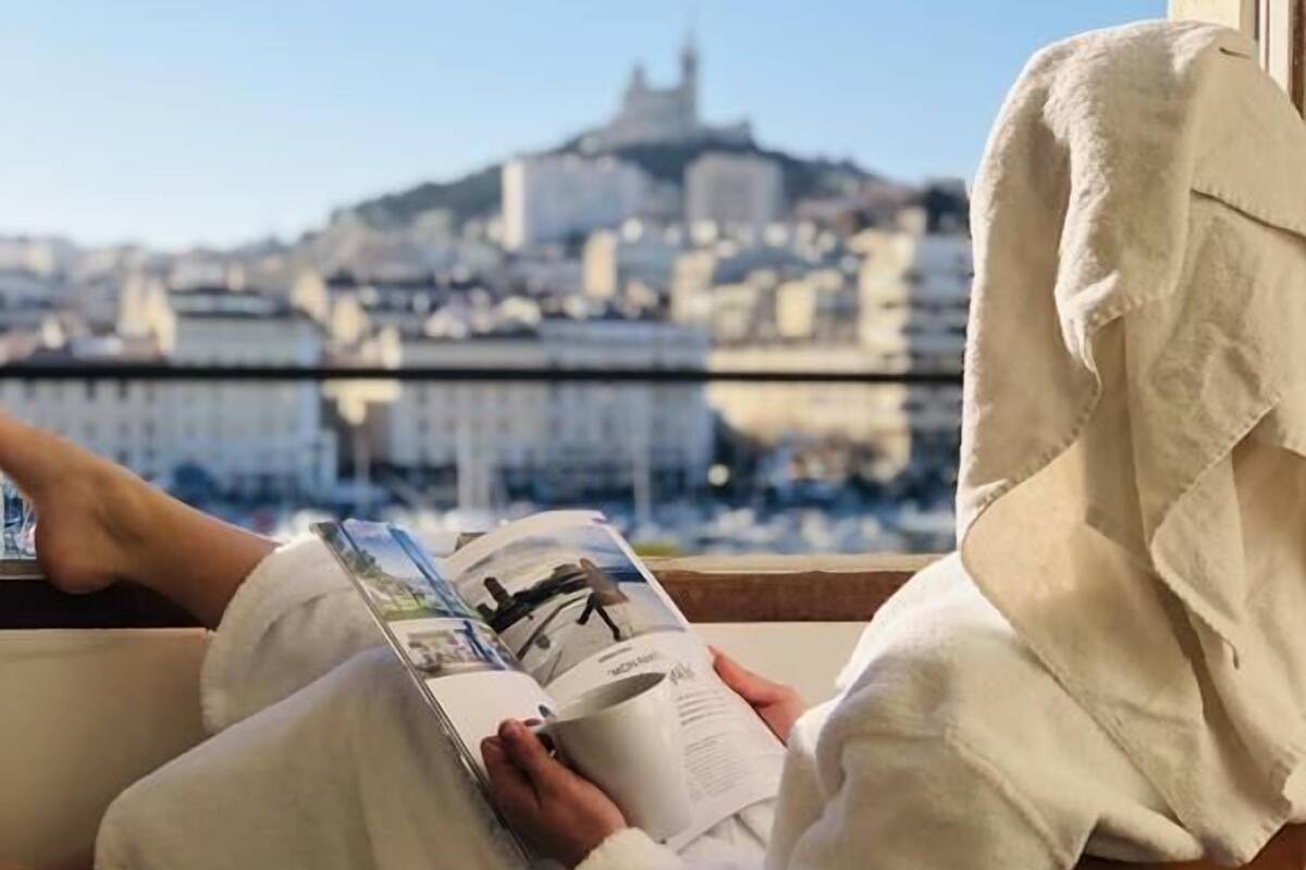 Une personne est assise dans un fauteuil près d’une fenêtre et lit un livre.