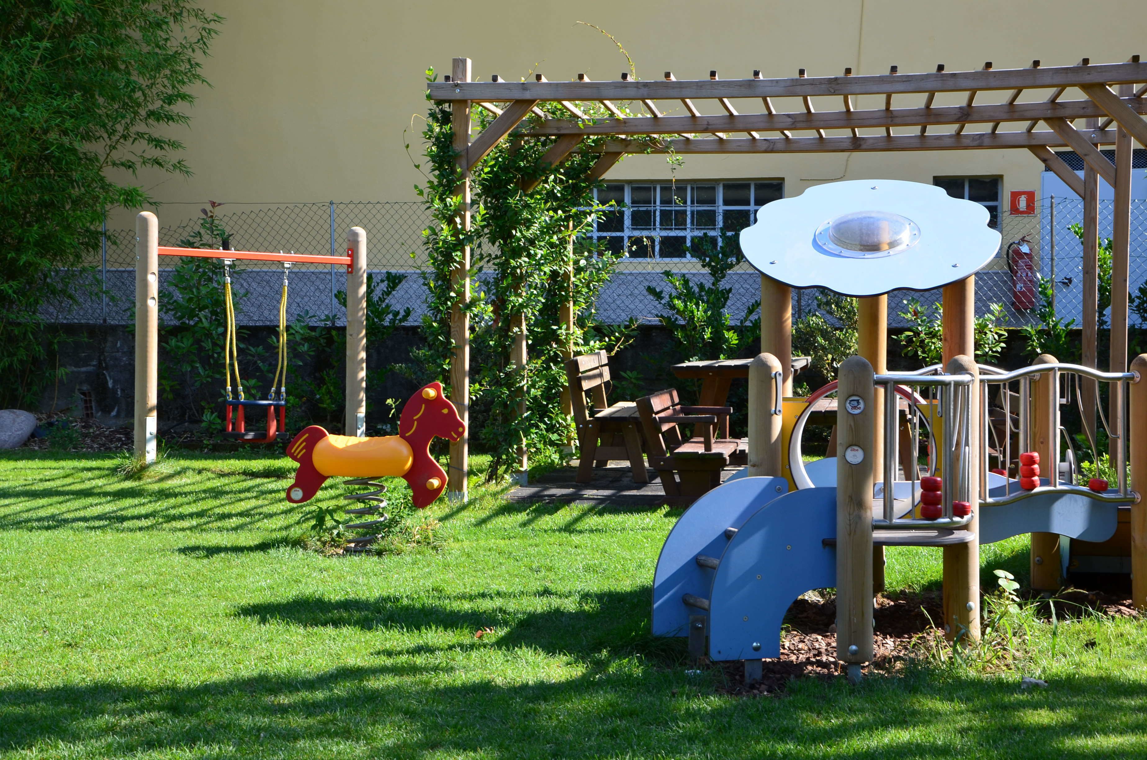 Ein Spielplatz mit einer hölzernen Kletterkonstruktion, Schaukeln und einem roten Spielzeugpferd.