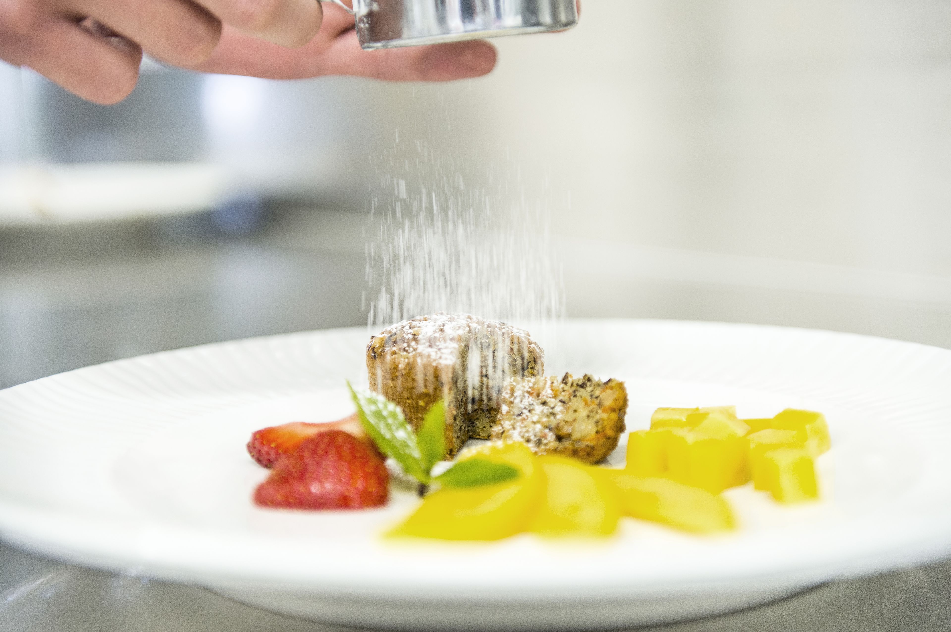 Une assiette de dessert avec une part de gâteau, des fraises et des morceaux de mangue.