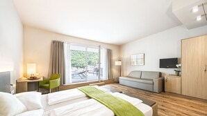 Een hotelkamer met twee bedden, een bank, een bureau met een lamp, een televisie en een schuifdeur naar buiten.