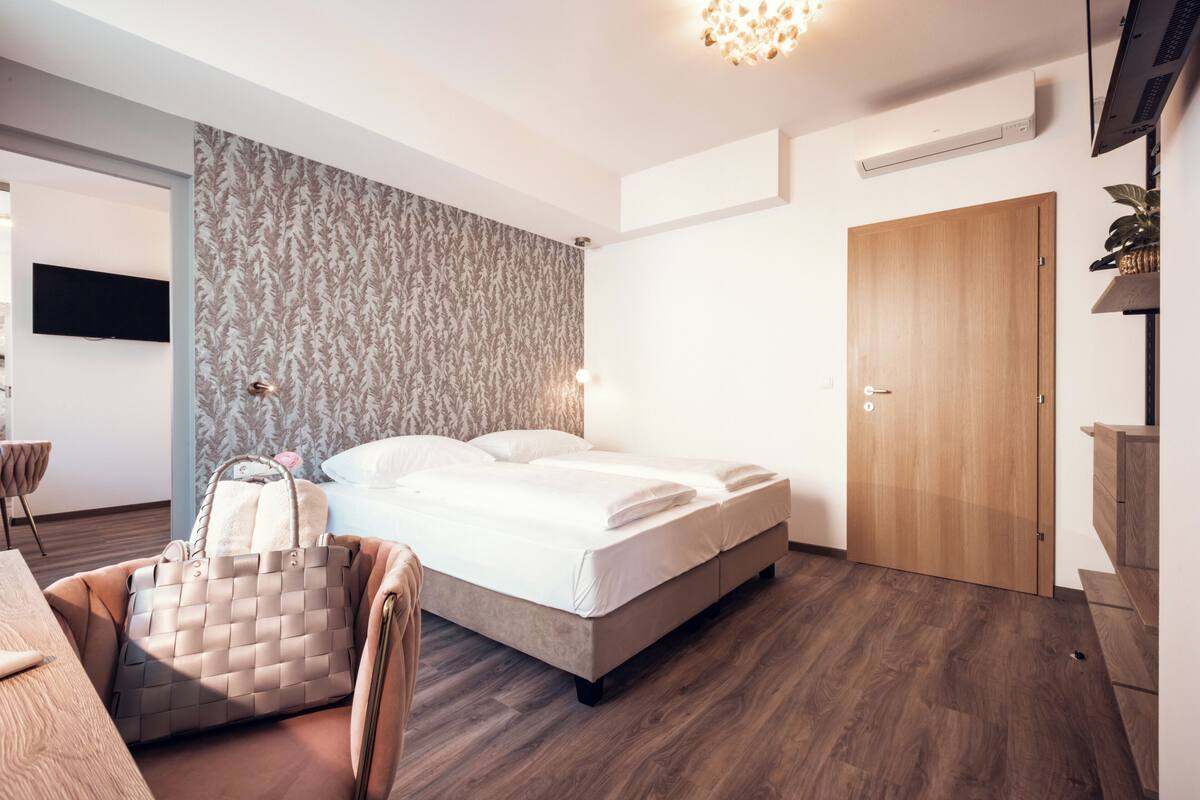 A modern bedroom with a bed, a wooden door, a wall-mounted TV, and a patterned wallpaper.