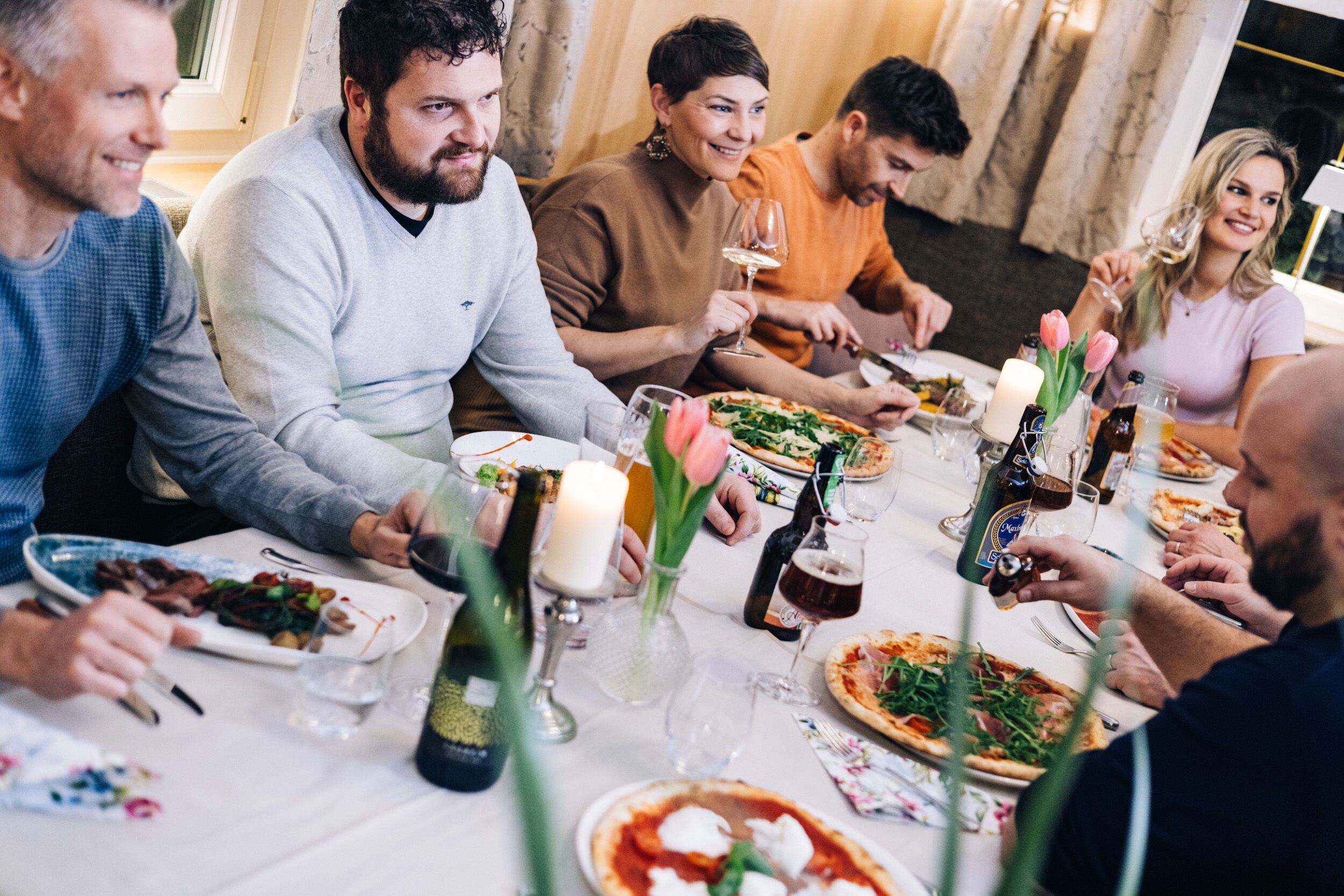 A group of people dining at a table with various dishes, glasses, and candles.