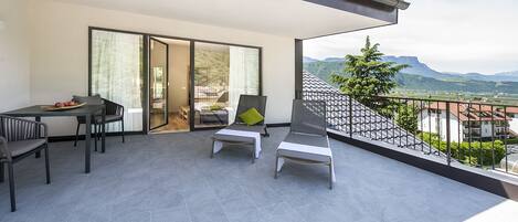 A balcony with a table and chairs, a bed, and a view of mountains.