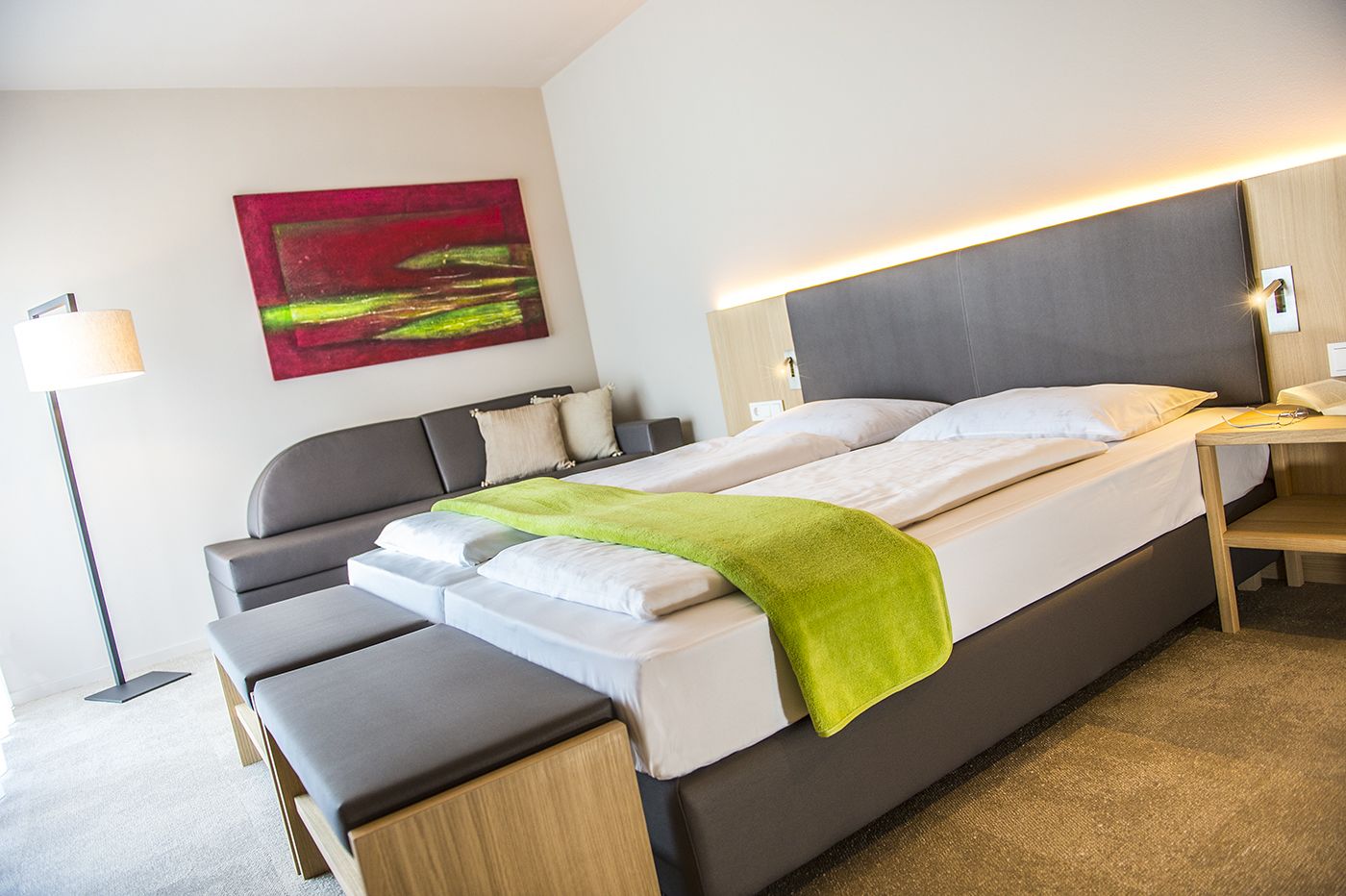 A modern hotel room with a large bed, bedside tables, a desk, and a floor lamp.