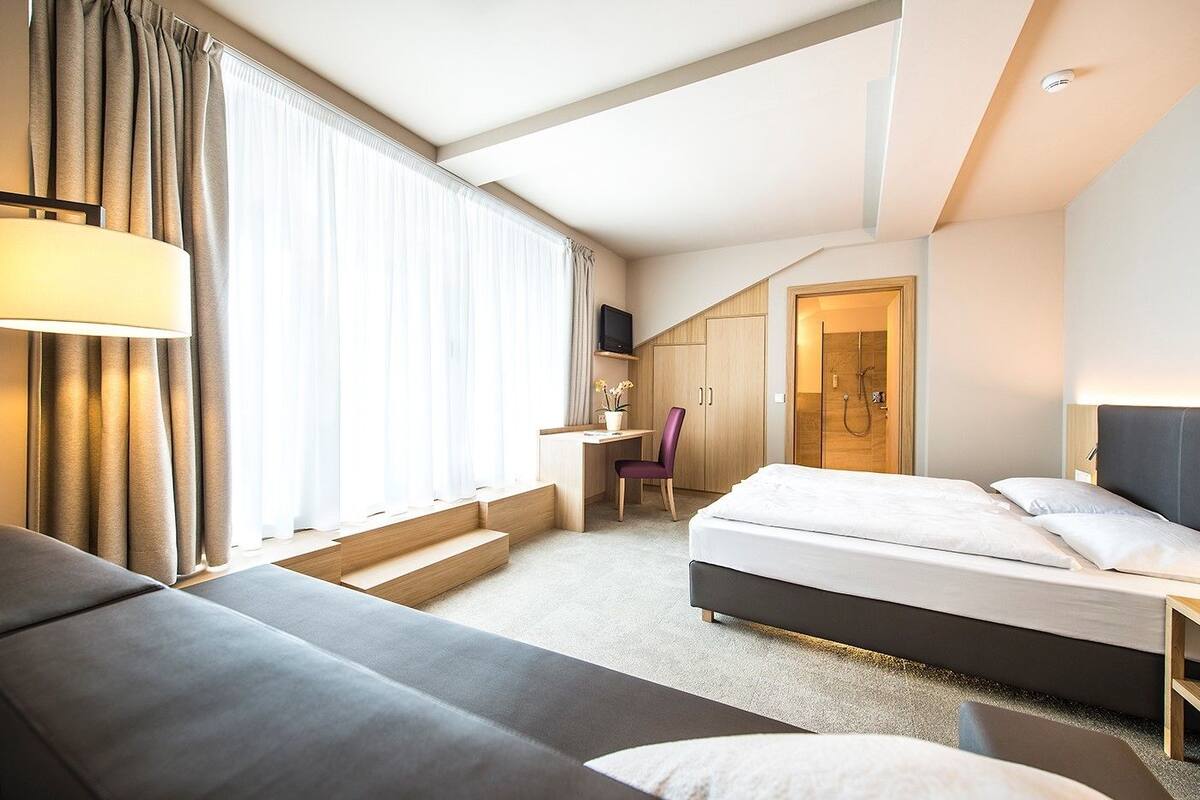 A hotel room with a bed, a desk, a chair, and a shower area.