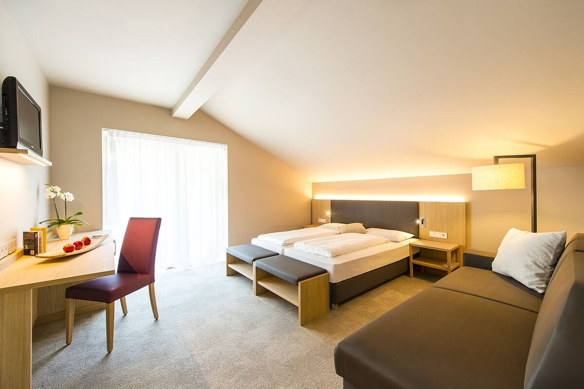 A hotel room with a bed, a desk, a chair, a sofa, and a TV.
