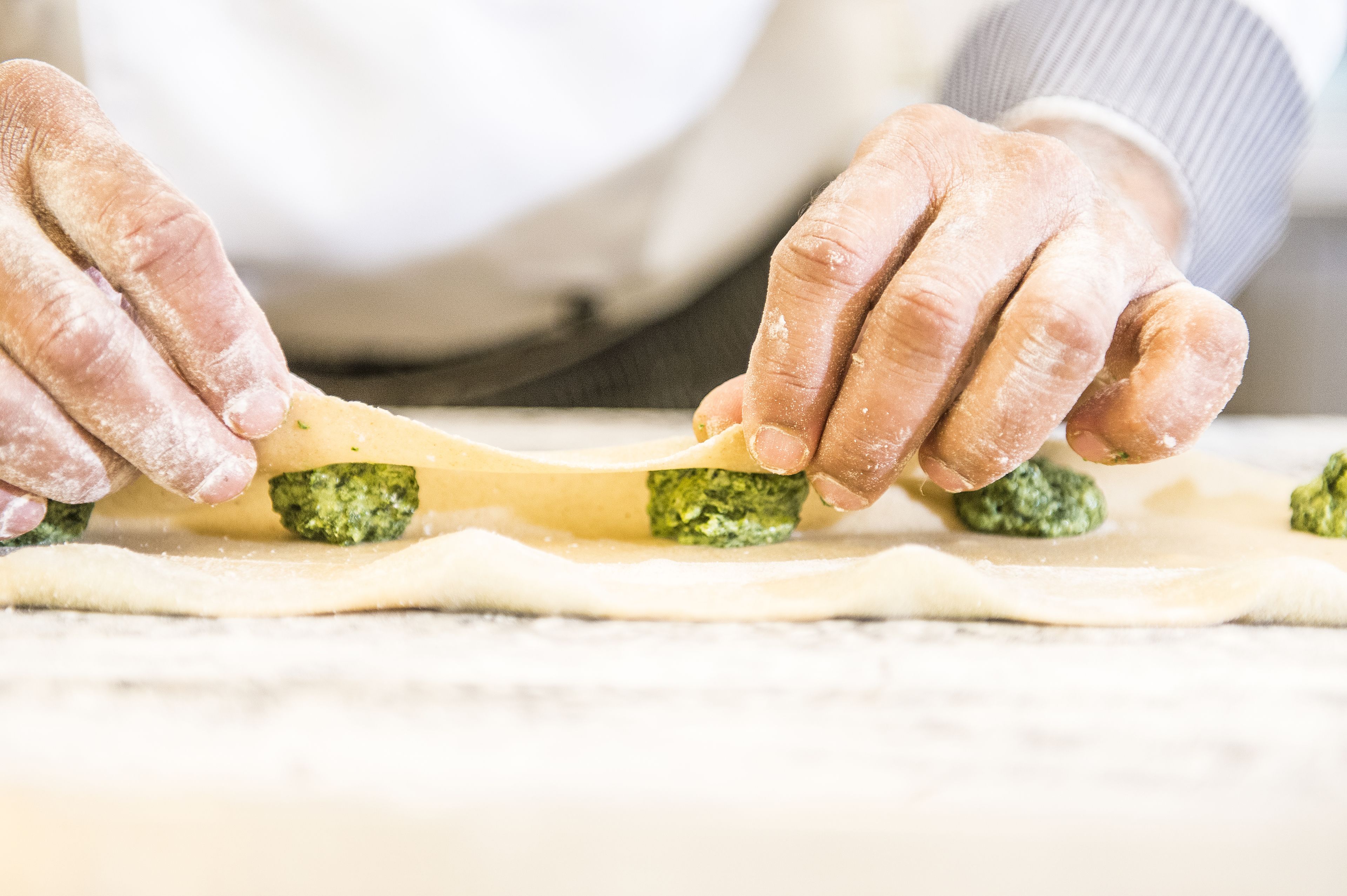 Hands preparing food, specifically rolling dough with green pesto and cheese.