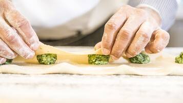 Hands preparing food, specifically rolling dough with green pesto and cheese.