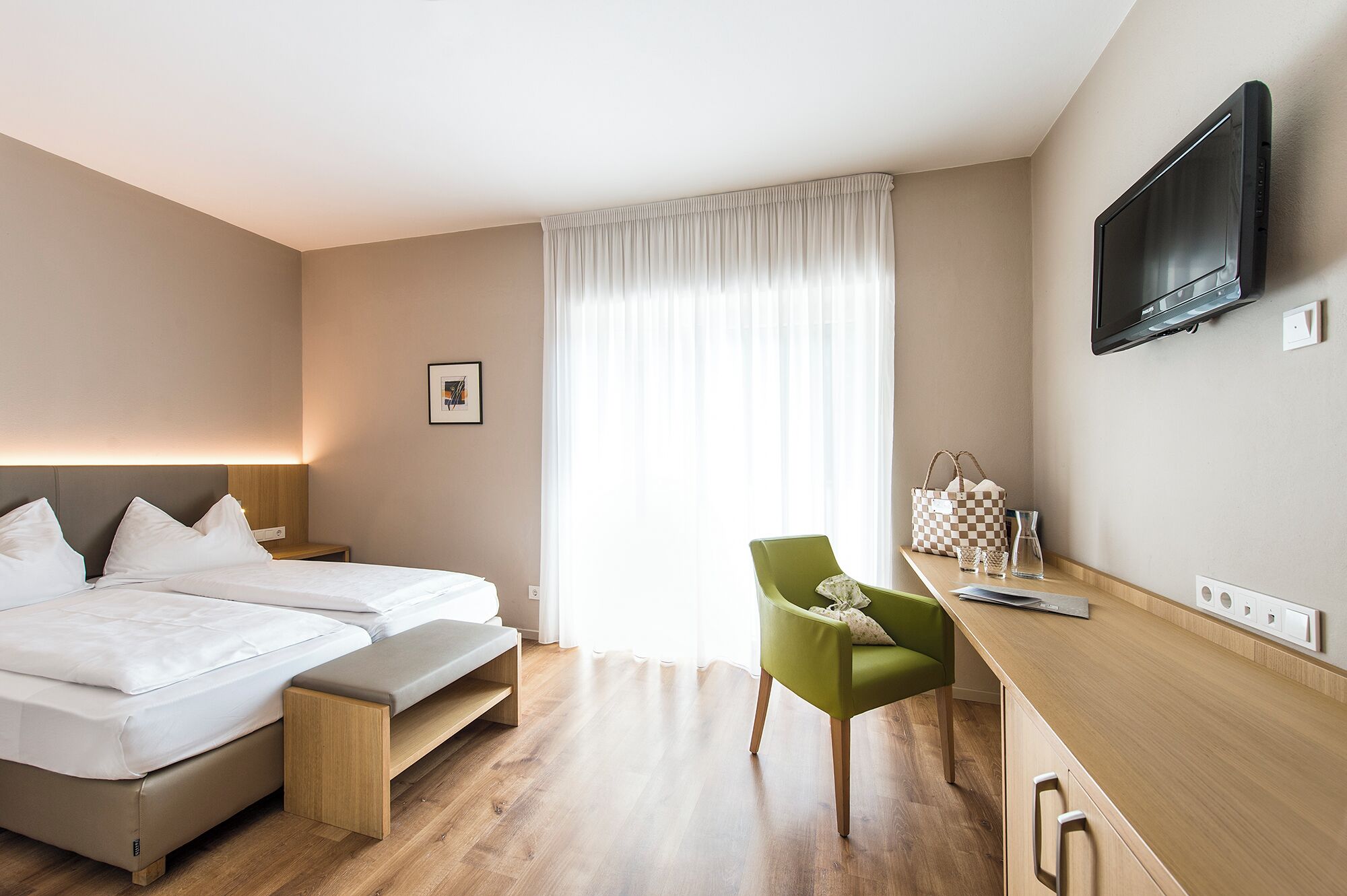 A hotel room with a bed, a desk, a chair, a TV, and a window with curtains.