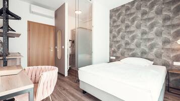 Una habitación de hotel moderna con cama, escritorio, silla, armario y zona de ducha.