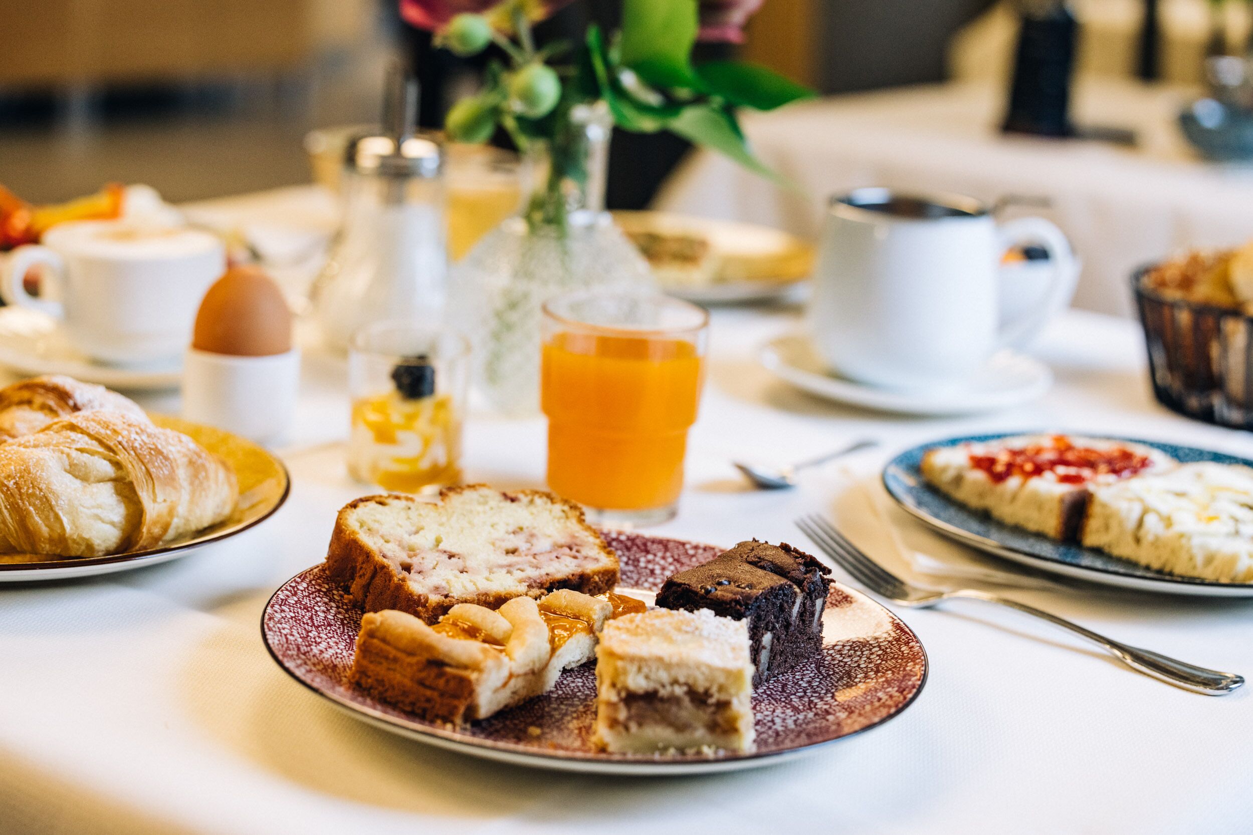 A breakfast setting with croissants, a slice of cake, and a glass of orange juice on a table.