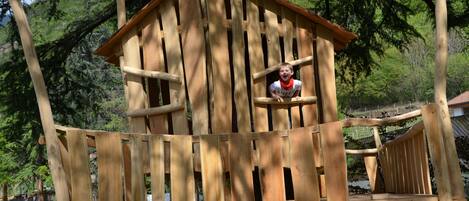 A wooden play structure with a house-like design, including a slide and climbing elements.