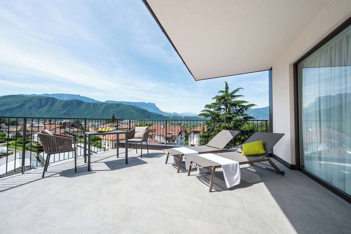 A balcony with a view of mountains, a table, and chairs.