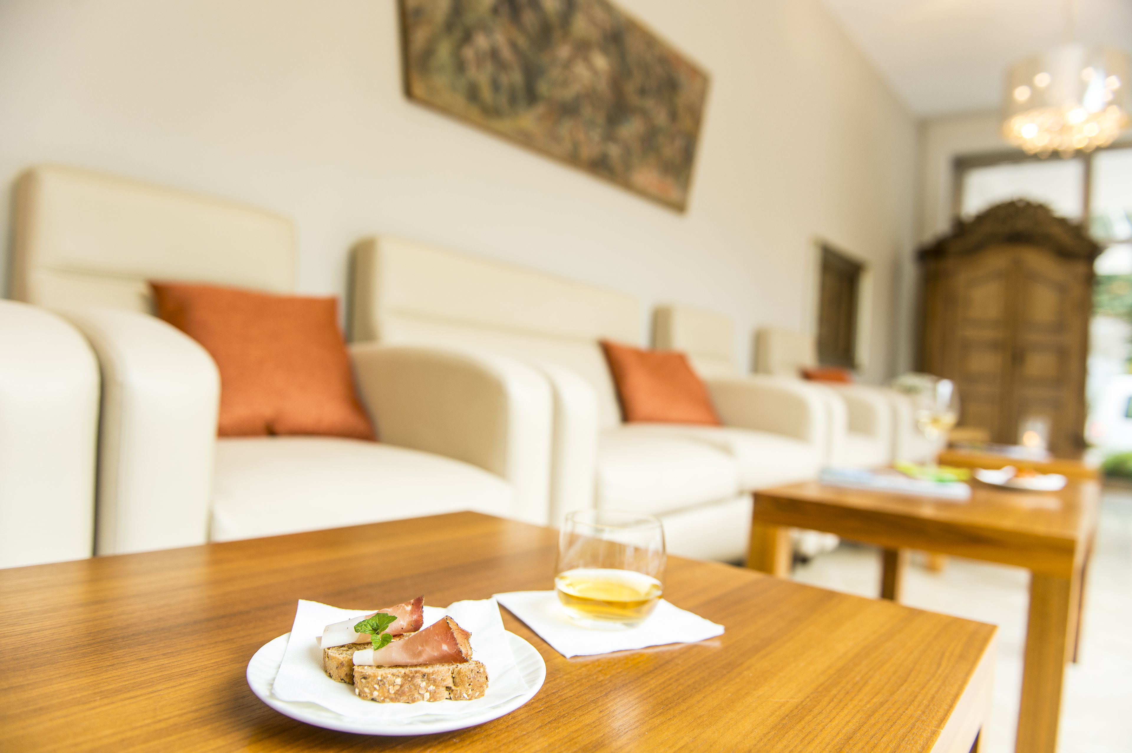 Ein Esstisch mit einem Teller Essen und einem Weinglas in einem Wohnzimmer, das eine Couch und ein Bild an der Wand umfasst.