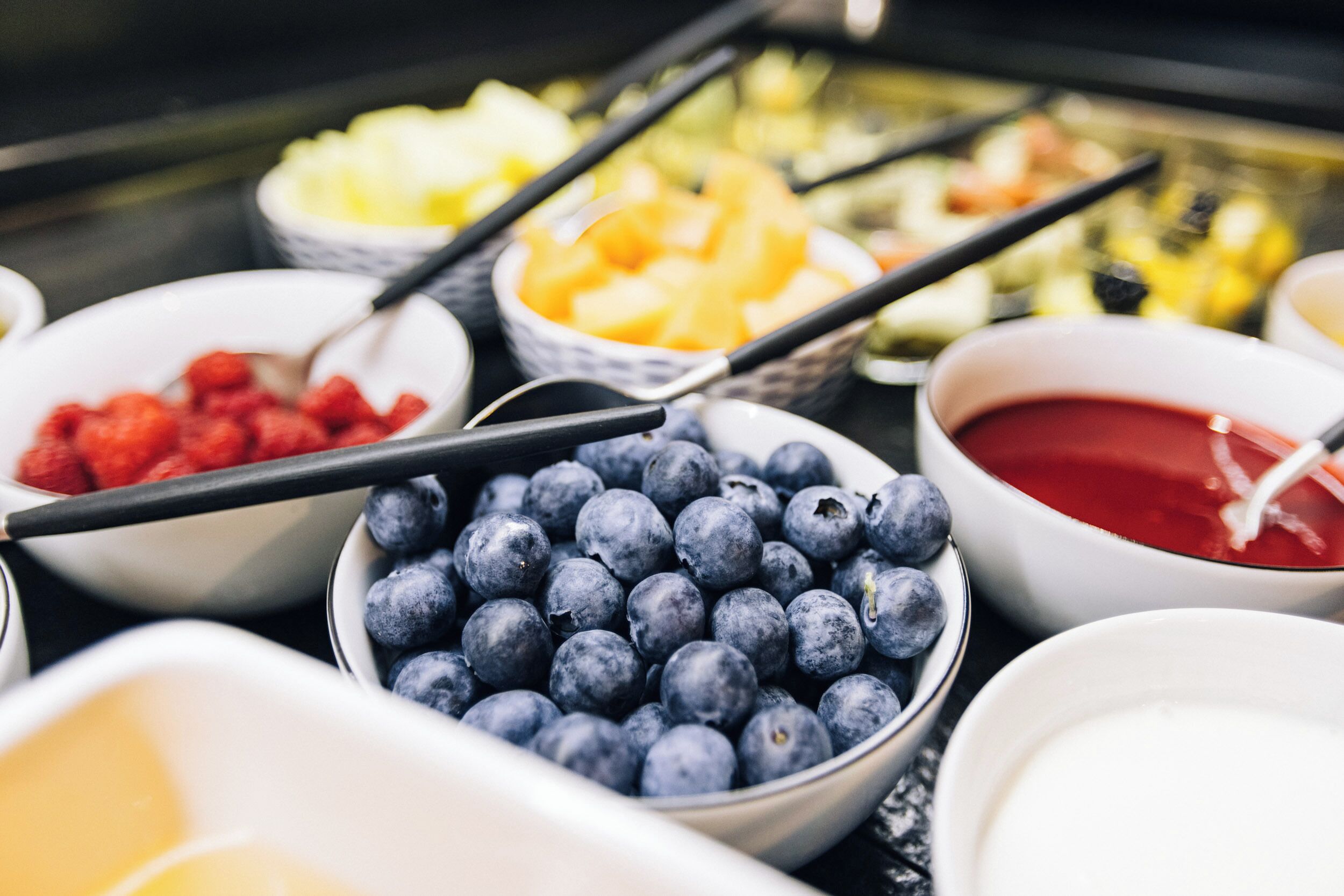 Diversas tigelas com frutas diferentes e um molho vermelho, com pauzinhos apoiados nelas.