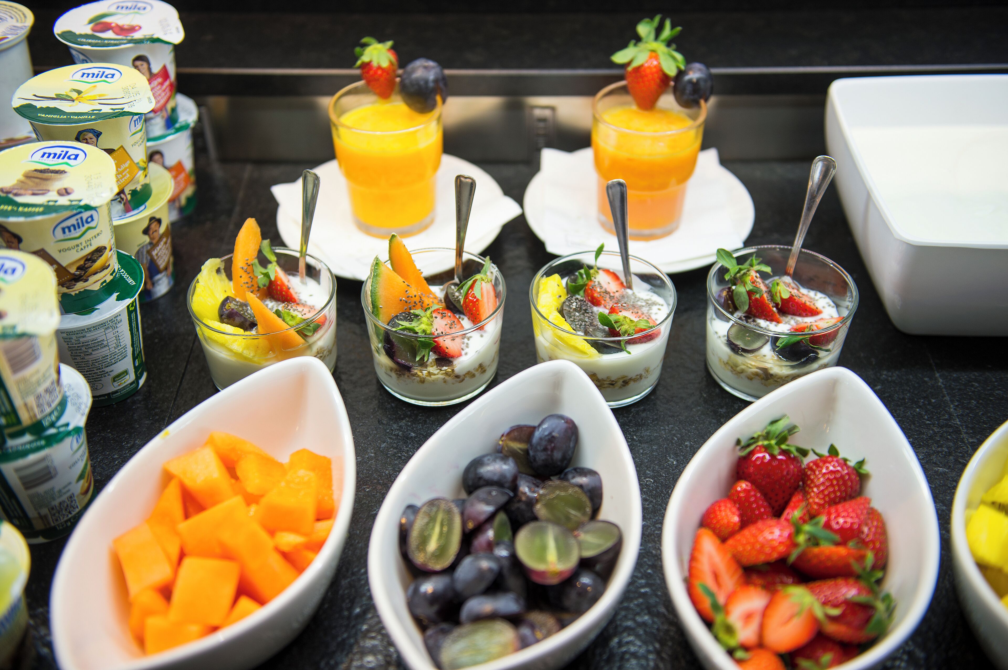 Un bufé de desayuno con diversas frutas, yogur y jugo de naranja.